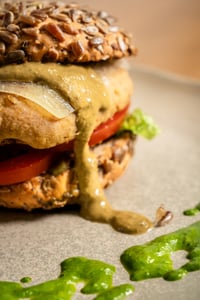 Hamburguesa vegetal de garbanzos y alubias servida en MATRICE Restaurante, con pan integral de semillas, rodajas de tomate