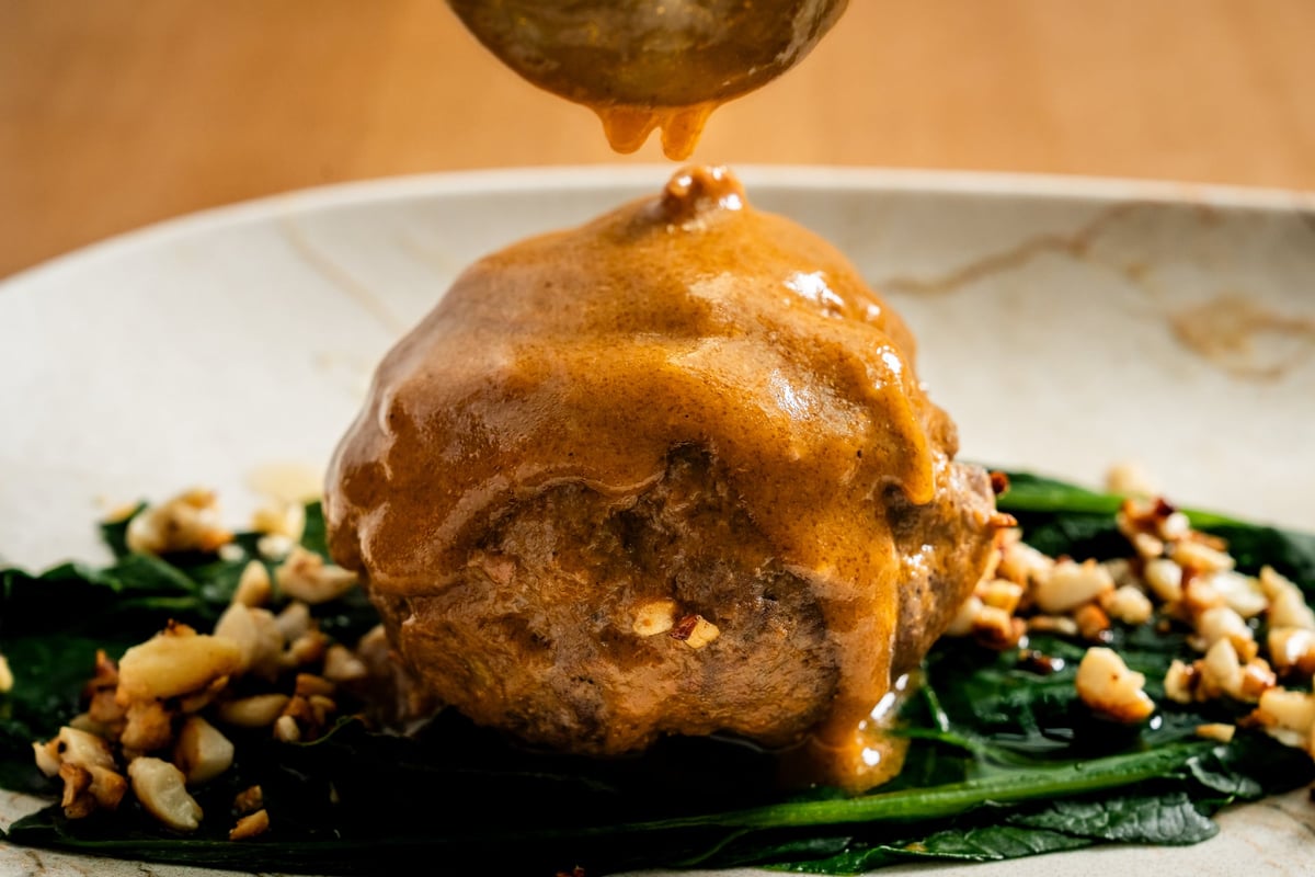 A juicy venison meatball smothered in a dark, glossy sauce is served on a bed of fresh spinach and chestnut pieces. The dish
