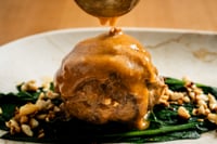 Une boulette de viande de cerf juteuse, nappée d’une sauce sombre et brillante, est présentée sur un lit d’épinards frais et