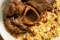 Ossobuco de veau servi dans une assiette, nappé d'une sauce épaisse et foncée agrémentée de morceaux de légumes et d'herbes