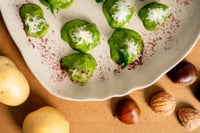 Chestnut gnocchi arranged on a wooden board, served with ingredients such as fresh sage leaves, grated cheese, and whole