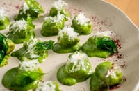 Chestnut gnocchi served on a rustic wooden board, topped with shavings of Parmesan cheese and accompanied by fresh arugula