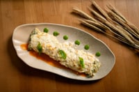 Plato de canelón relleno de espinacas y queso, gratinado con salsa y decorado con hojas de menta fresca y granos de pimienta