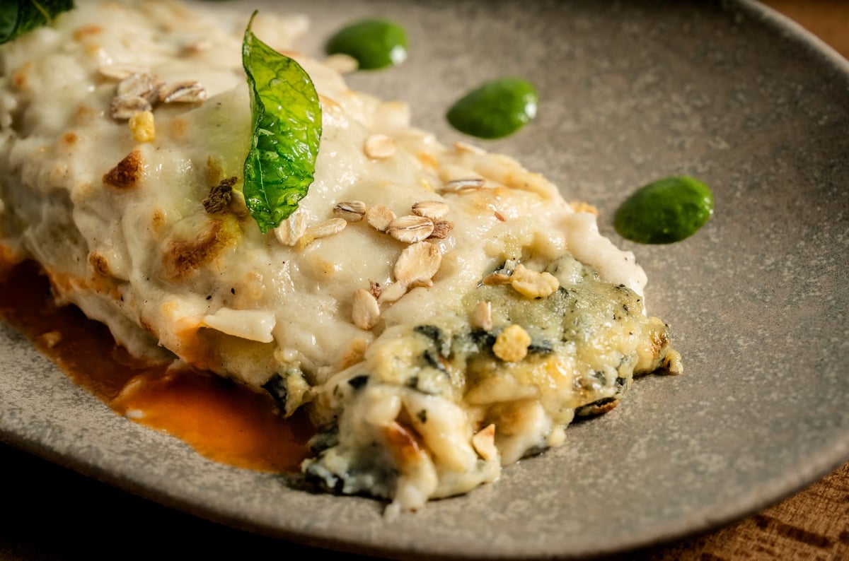 Canelón relleno de espinacas y queso gratinado, servido en una tabla de madera rústica. La superficie dorada y crujiente